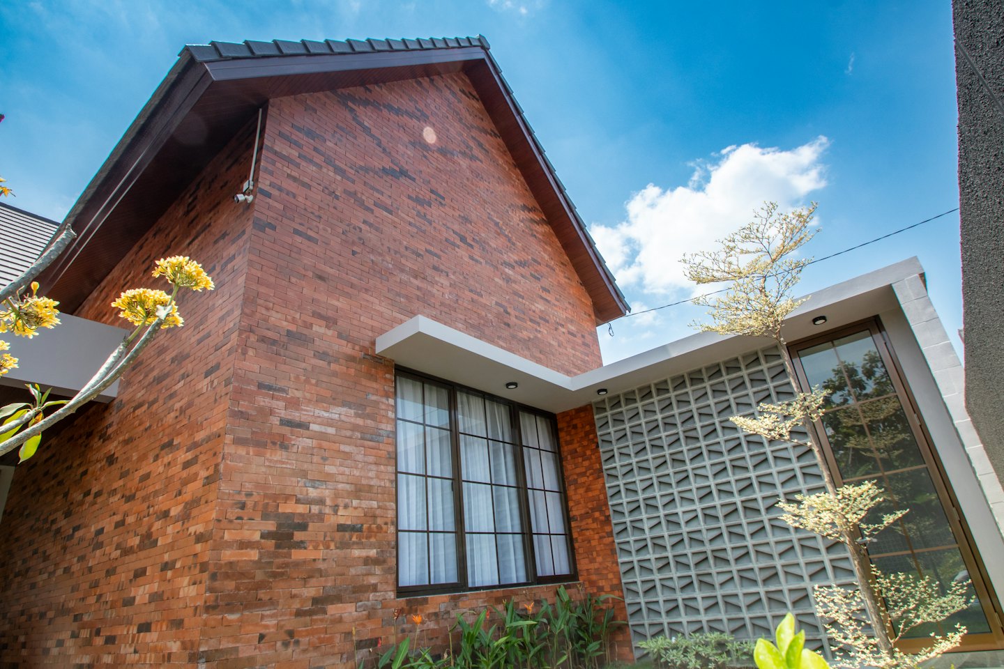 Modern red brick house with large windows under blue sky.